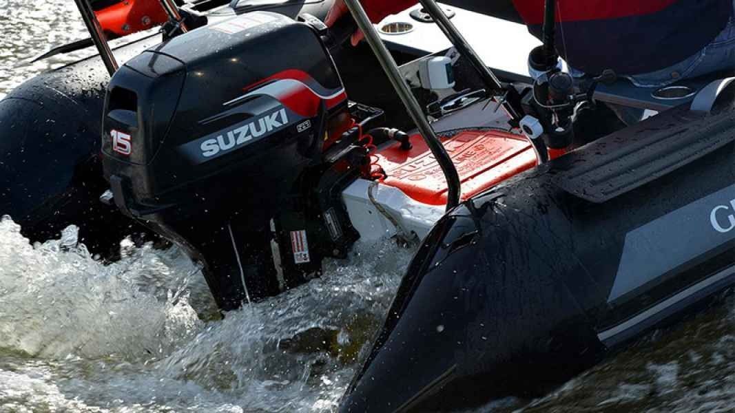 Black Suzuki outboard motor powering a red boat through splashing water