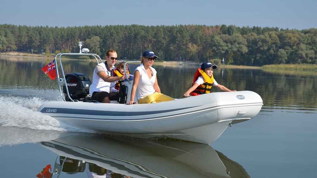 Inflatable boat with three people cruising on a calm lake, leaving a white wake behind.