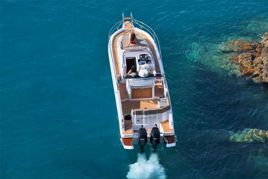Top-down view of a white ranieri 370 executive speedboat on blue water, leaving a foamy wake near rocky shore