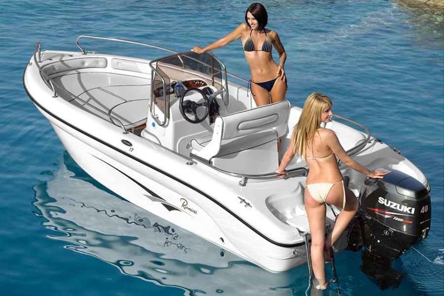 Two women in swimsuits on a small motorboat at sea, one boarding near the outboard motor.