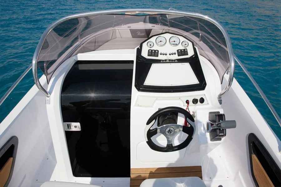 Boat cockpit with steering wheel and dashboard under a clear windshield on open water.