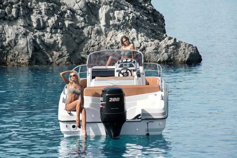 Two people on a white Ranieri Voager 23s motorboat near rocky cliffs in calm blue water