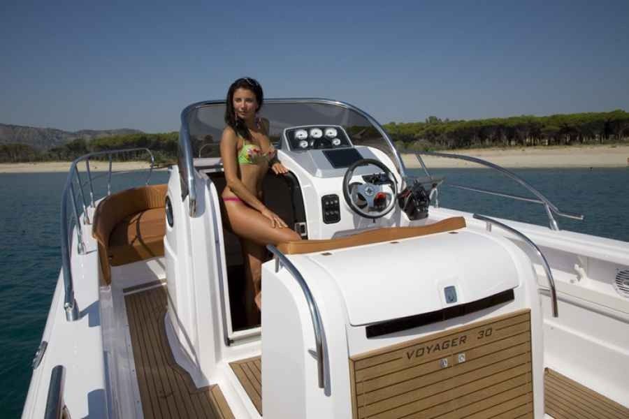 Woman sitting on a white speedboat at a sunny marina, with blue water and shoreline in the background