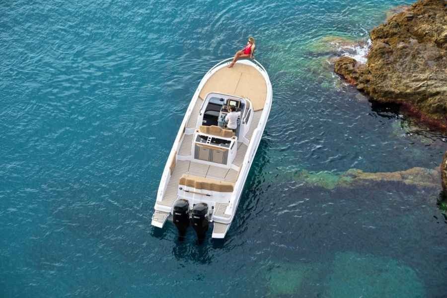 White speedboat with twin outboard motors floating in clear blue water near a rocky shore