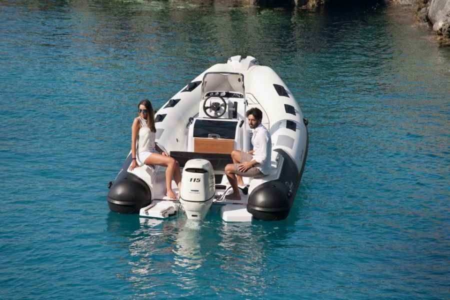 Two people on a small white motorboat floating on clear blue water