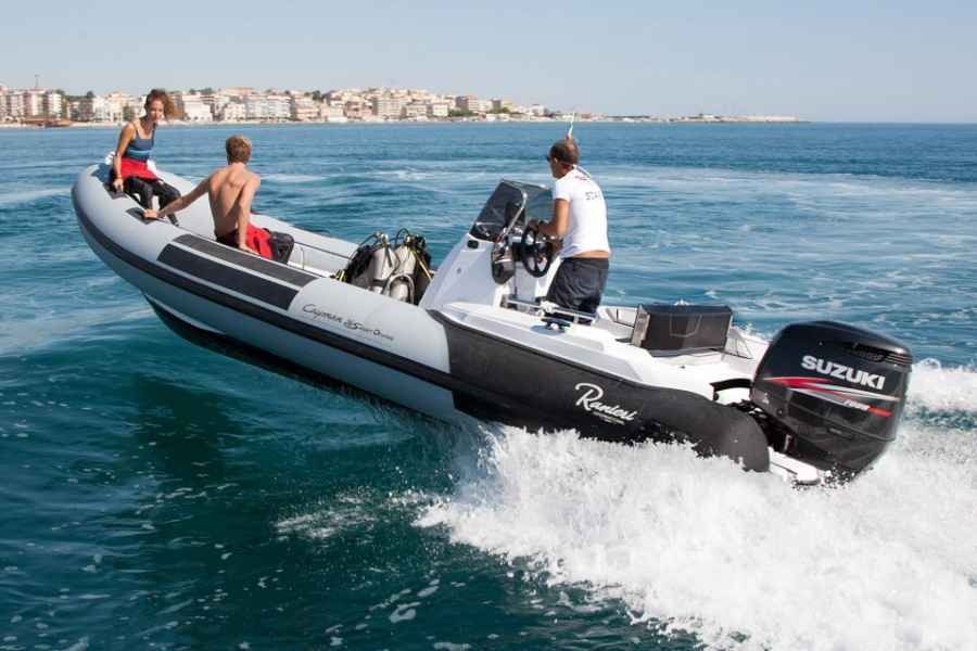 Three people on a ranieri cayman 26 sport diving rib speedboat racing across choppy blue water near a distant shoreline