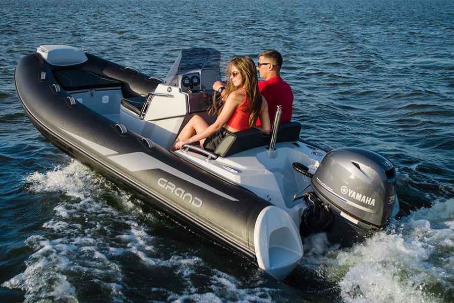 Two people riding a black inflatable speedboat on choppy water, with a Yamaha outboard motor.