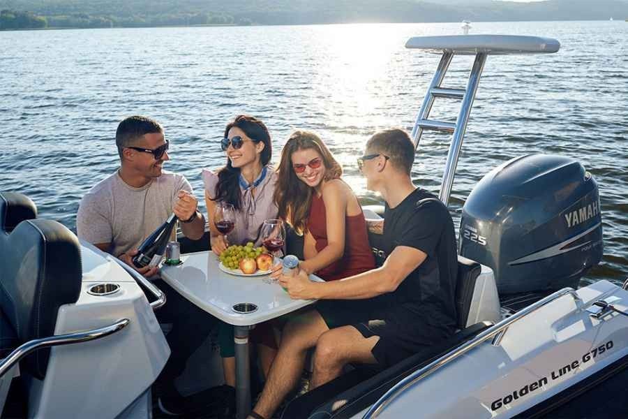 Four friends share drinks at a table on a motorboat on calm water at sunset