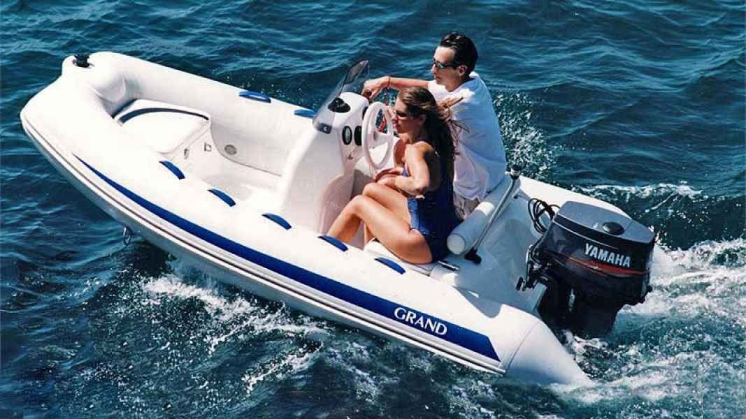 Two people riding in a white inflatable boat on blue water, with a motor at the back.