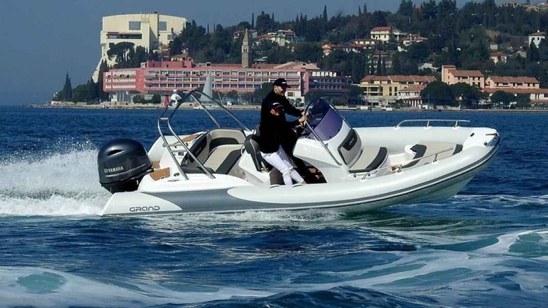 White grand golden line 580 motorboat speeding on choppy water near a coastal town and hillside buildings