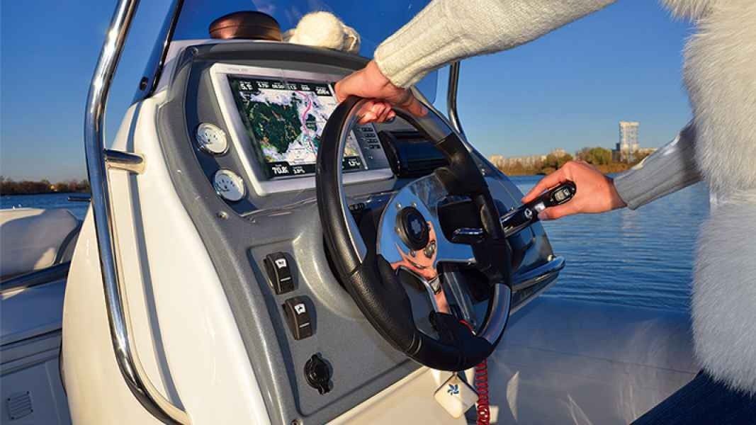 Person steering a boat at sunset, with hands on the wheel and calm water in the background