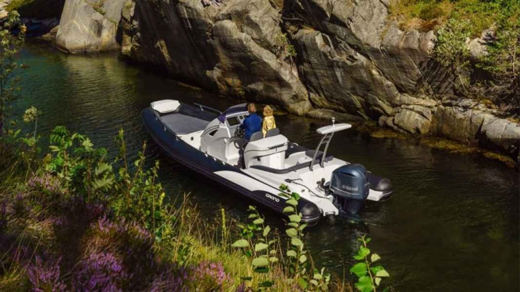 Small white motorboat floating on a calm rocky creek beside overhanging trees and greenery