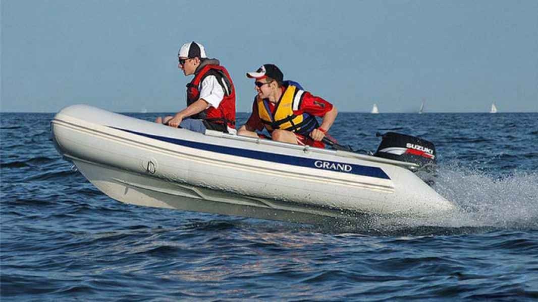 Two people in life jackets ride an inflatable grand silver line 300 speedboat on choppy blue water.