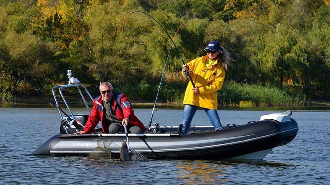 Two people in a black grand silver line 370 inflatable boat on a lake, one steering and one standing in a yellow jacket
