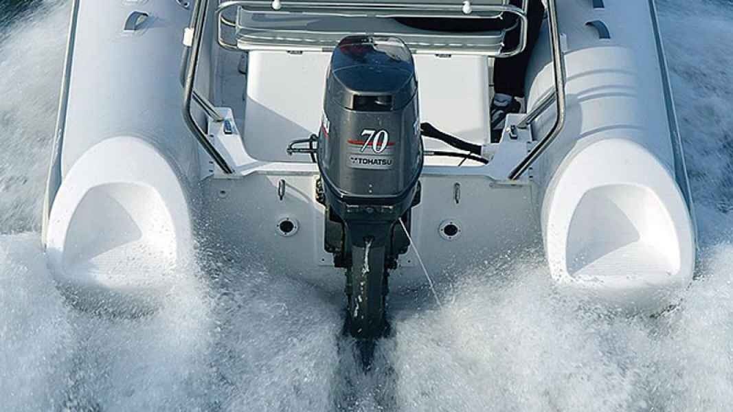 Outboard motor powering a small boat through choppy white spray on water