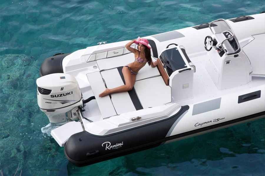 Woman relaxing on a white ranieri cayman 23 sport motorboat in turquoise water, wearing a pink hat.