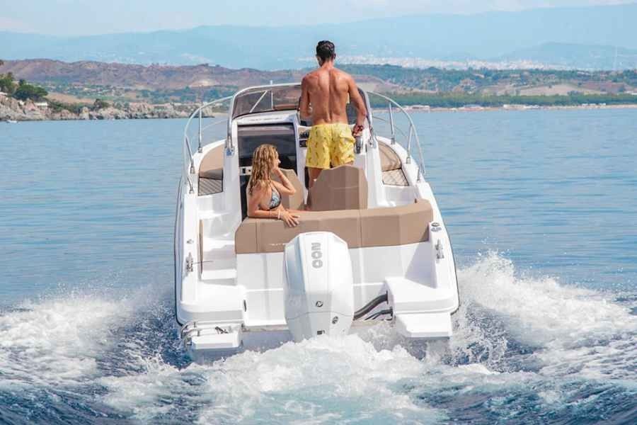 People on a white motorboat speeding across blue water near a coastal town