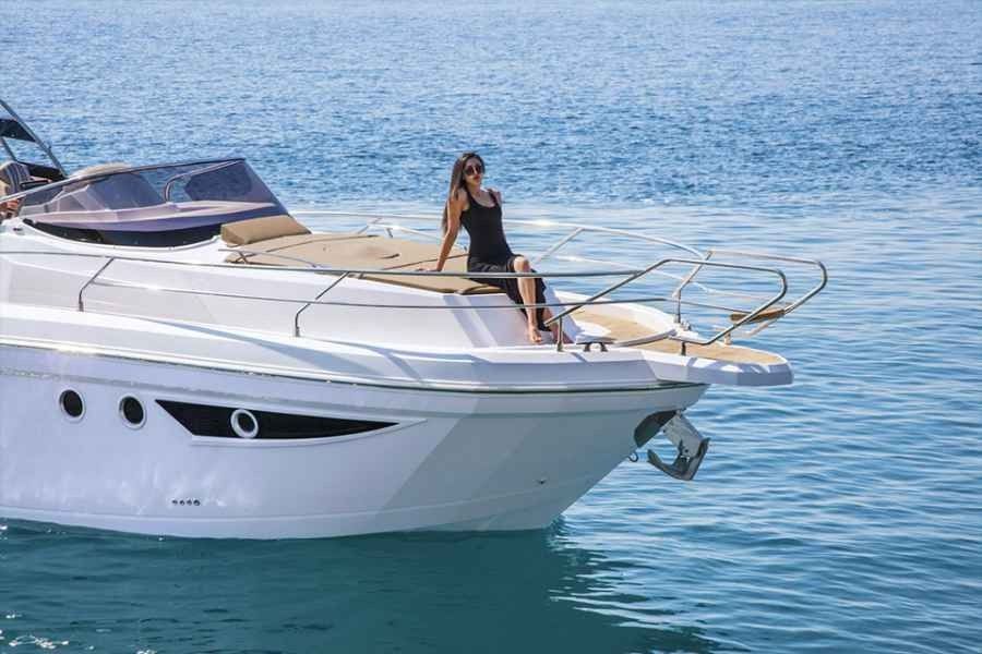 White boat on calm blue water with a person standing on the bow under a clear sky