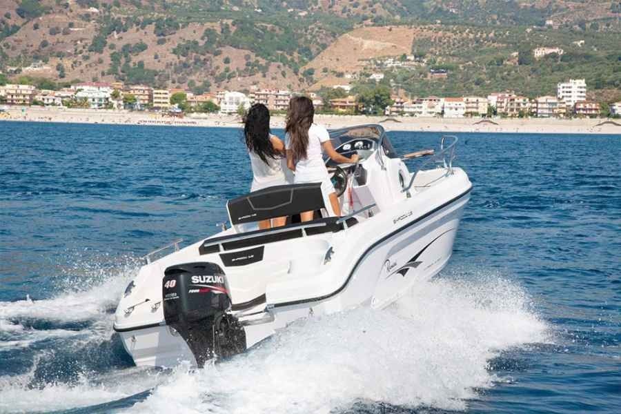 White speedboat racing on blue water with two people aboard, coastal town and hills in the background