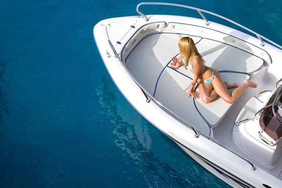 Woman reclining on the bow of a white motorboat in bright blue water.