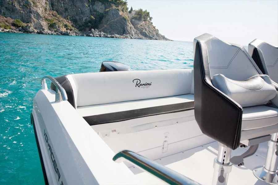 White luxury boat with gray seats on turquoise water near rocky coastline
