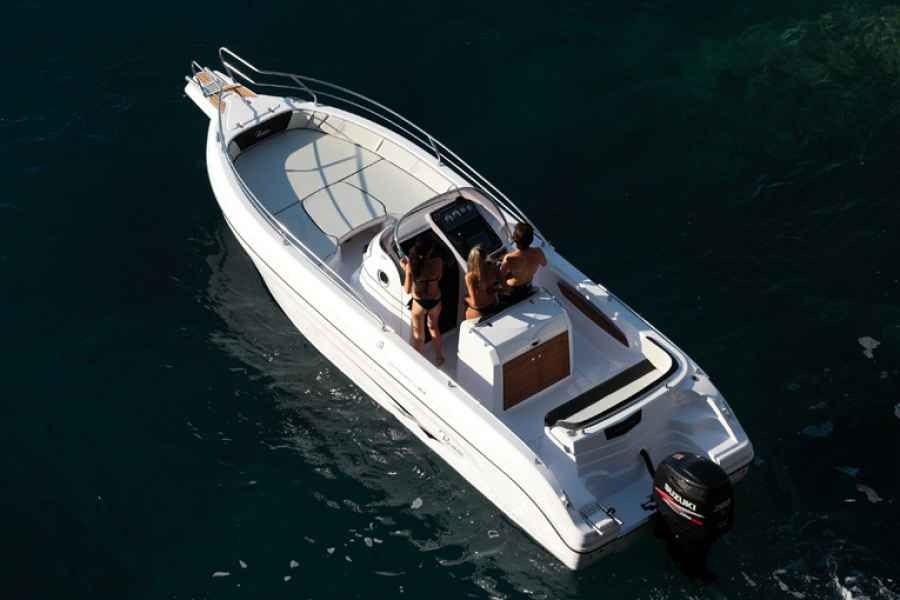 White motor yacht cruising on dark water, seen from above with two people on deck