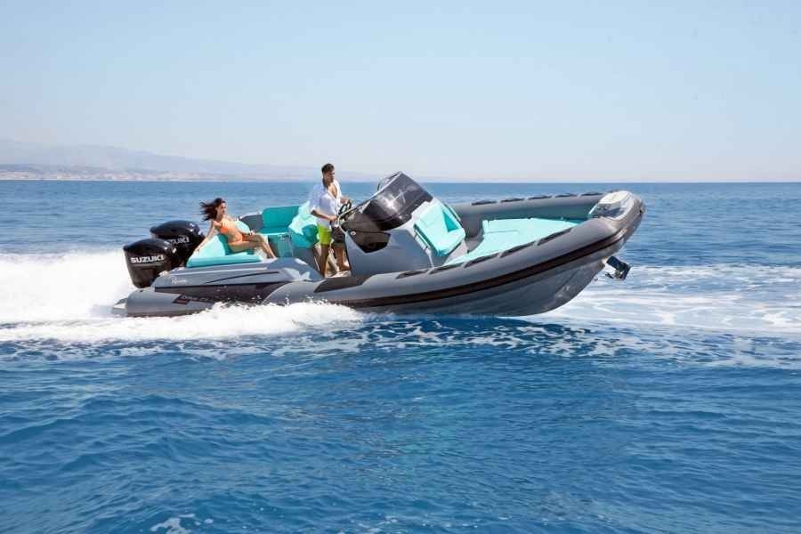 Two people riding a black and gray inflatable speedboat on calm blue water.