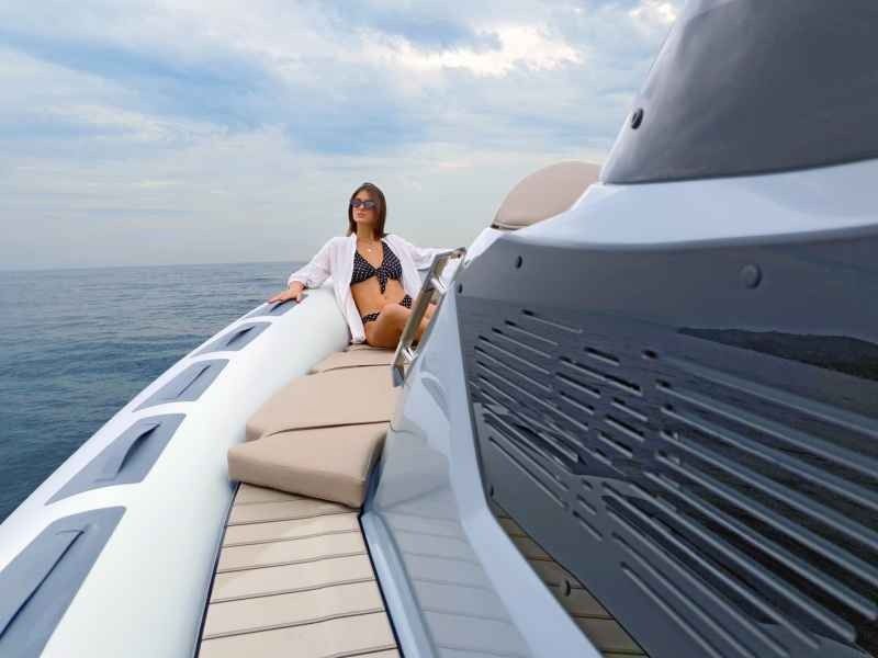 Person sitting on a yacht deck near the bow, with open sea and cloudy sky in the background.