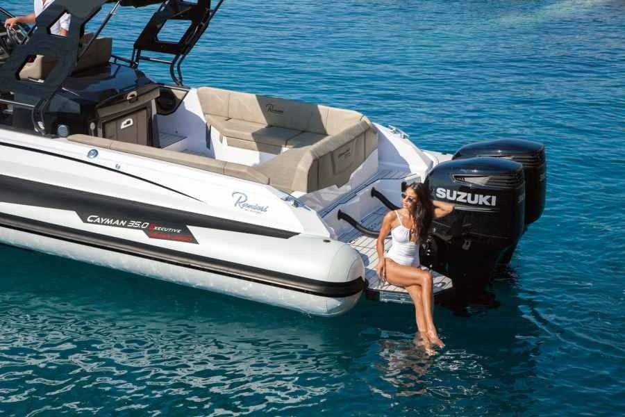 Woman dangling feet in the water beside a white boat and Suzuki outboard motor on turquoise sea