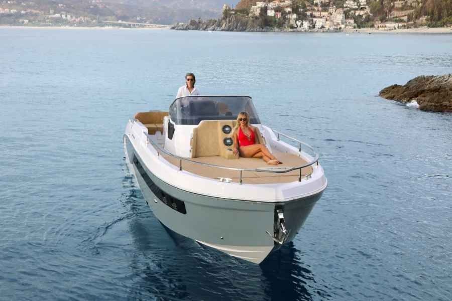A white Ranieri next 330 speedboat on calm blue water with two people aboard near a rocky coastline.