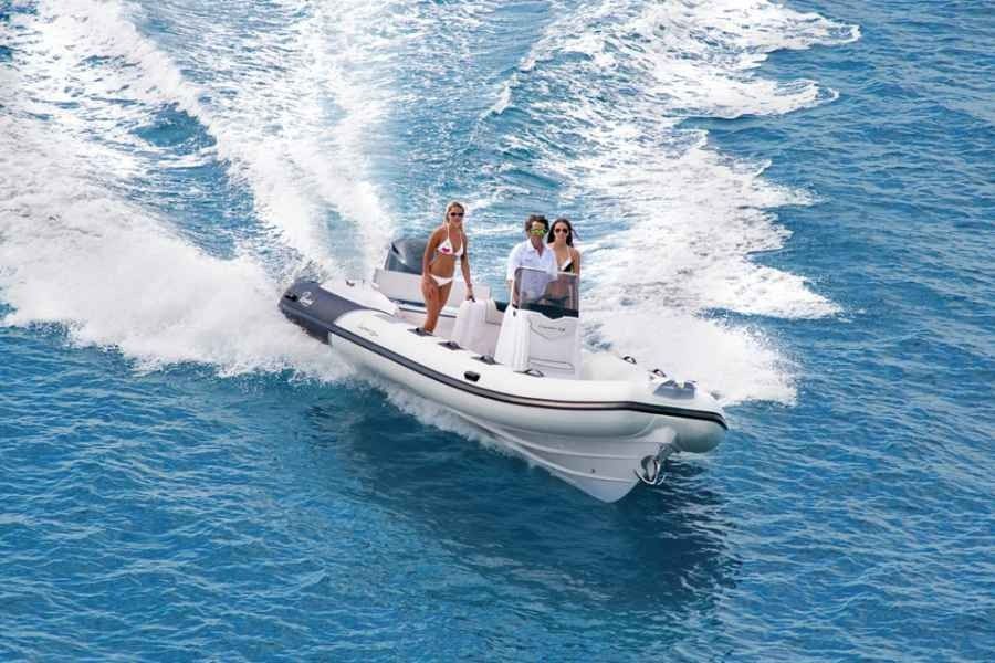 Three people riding a white ranieri cayman 26 sport speedboat, splashing across bright blue water.