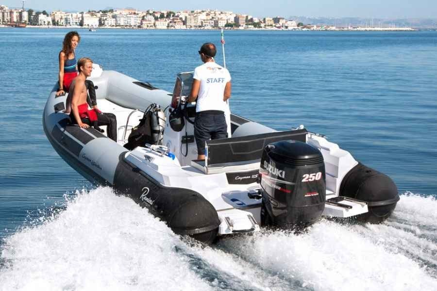 People riding a gray ranieri cayman 26 sport diving rib speedboat on calm blue water near a coastal town
