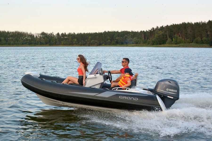 Two people riding a black grand golden line 420 inflatable motorboat on a lake, leaving a wake behind.