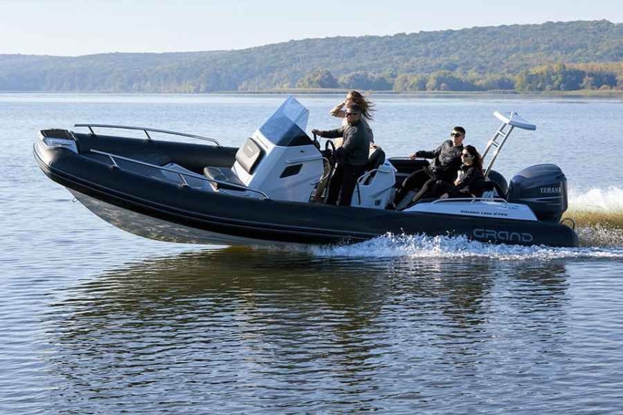 Black motorboat speeding on a calm lake with two people aboard near a wooded shoreline
