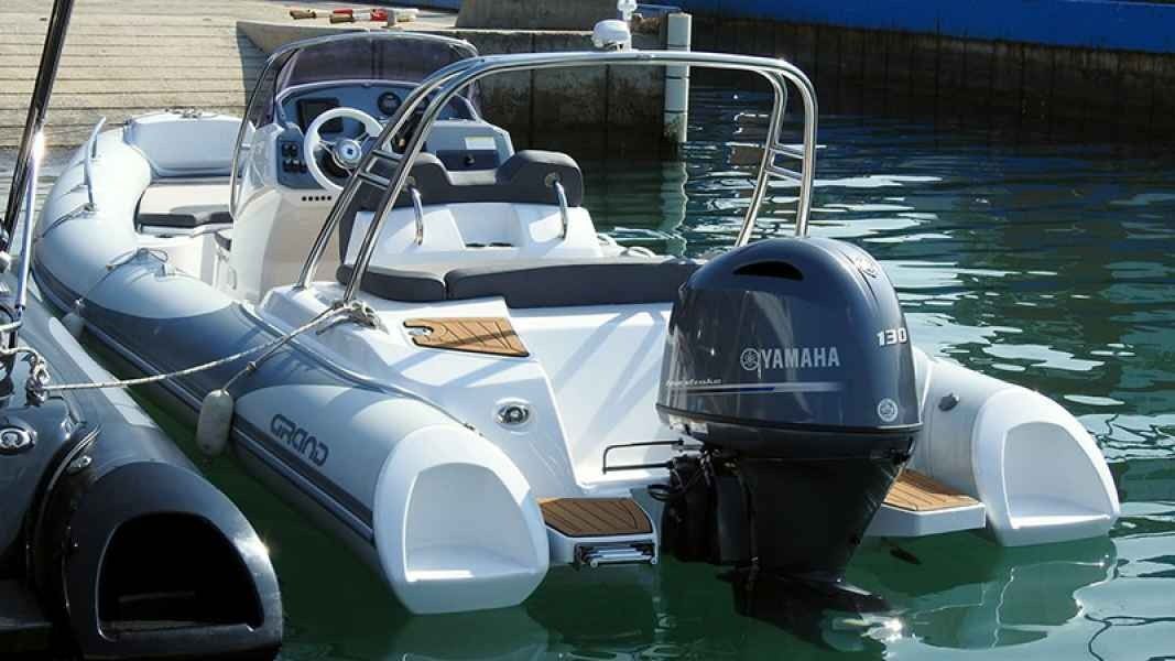 White grand golden line 580 inflatable motorboat docked on calm water, with a black outboard engine and steering console.