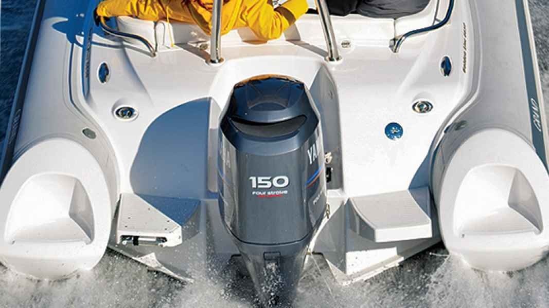 Rear view of a white boat with twin seats and a gray 150 hp outboard motor running in water