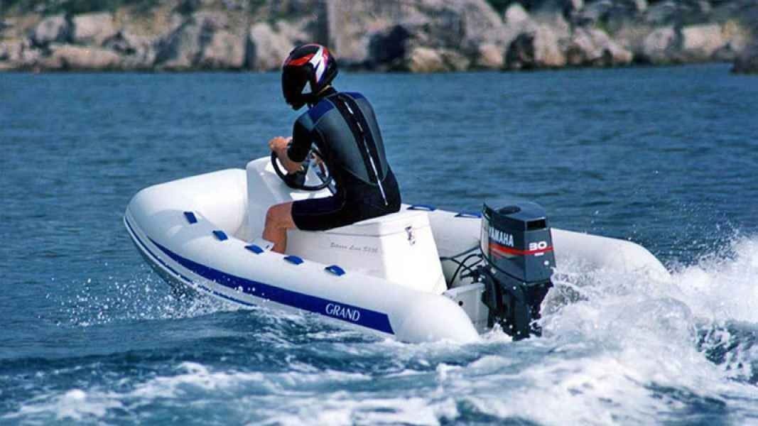Person riding a white inflatable grand silver line 300 boat across blue water near a rocky shoreline