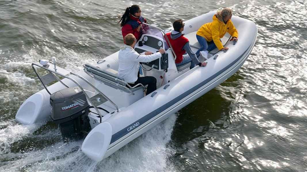 Four people ride in a gray inflatable motorboat speeding over choppy water
