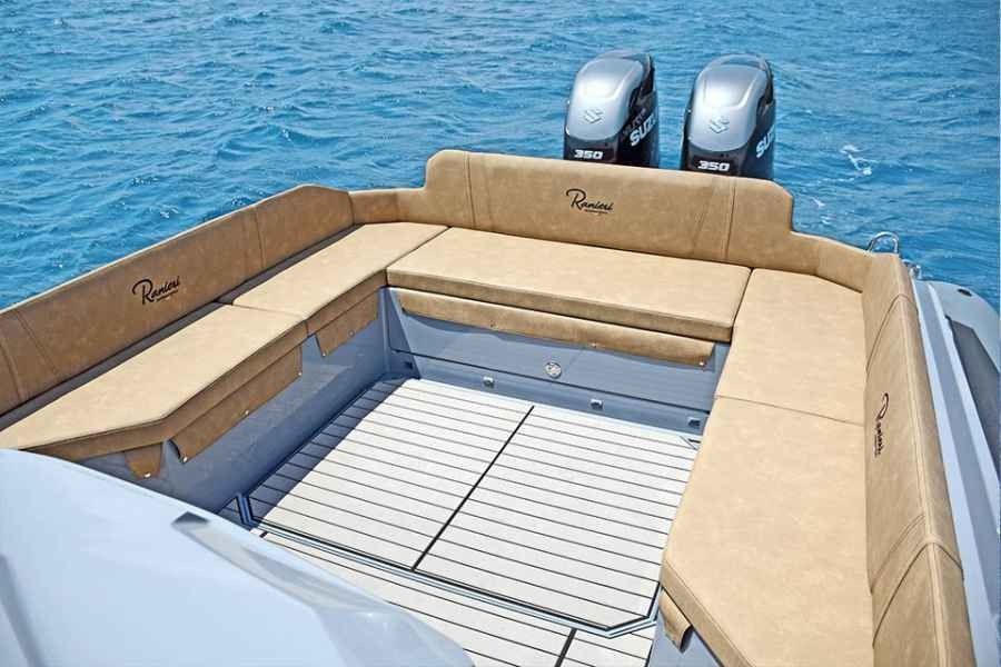 Luxury boat stern seating area with beige cushions and two outboard motors on blue water.