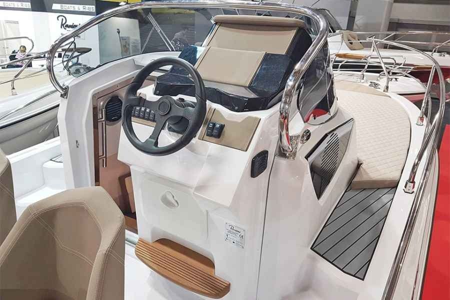 Ranieri next 240 Boat helm console with steering wheel, display, and tan-and-white seating inside a marina showroom