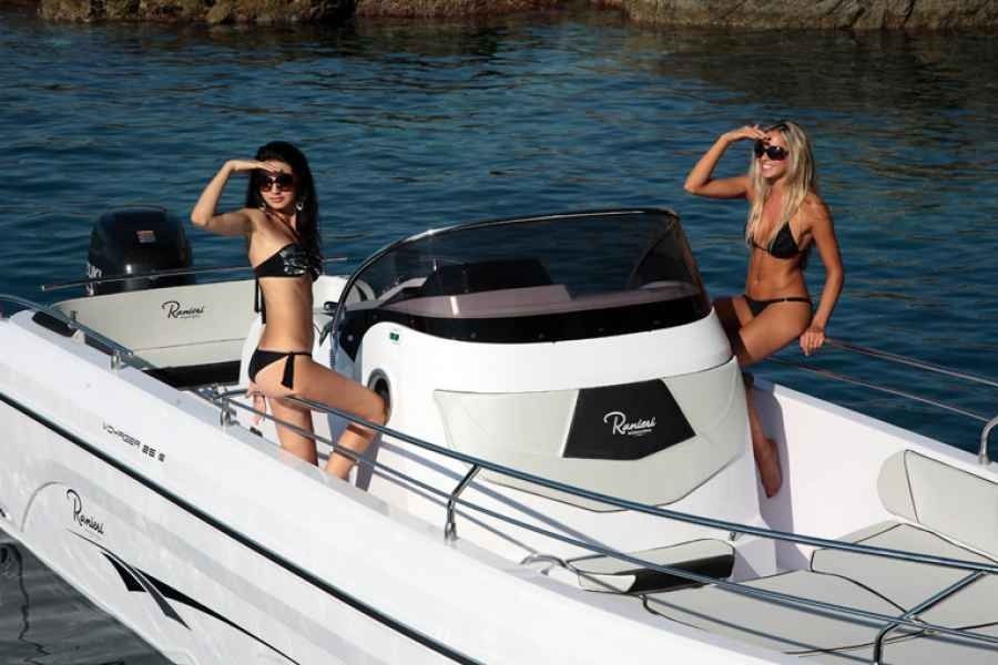 Two people in bikinis sunbathe on a white boat with a black canopy on blue water.