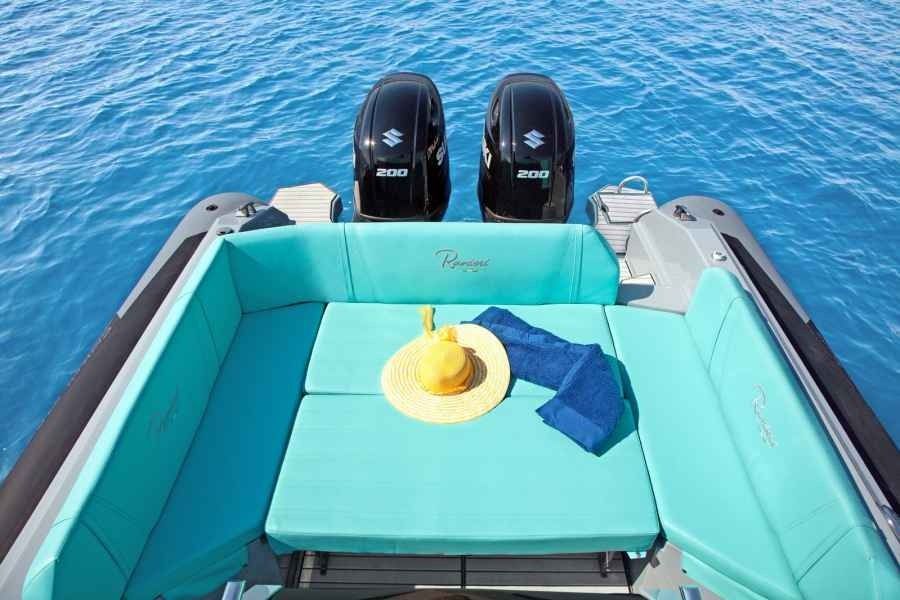 Turquoise boat seating with a yellow hat on deck, facing two outboard motors on blue water