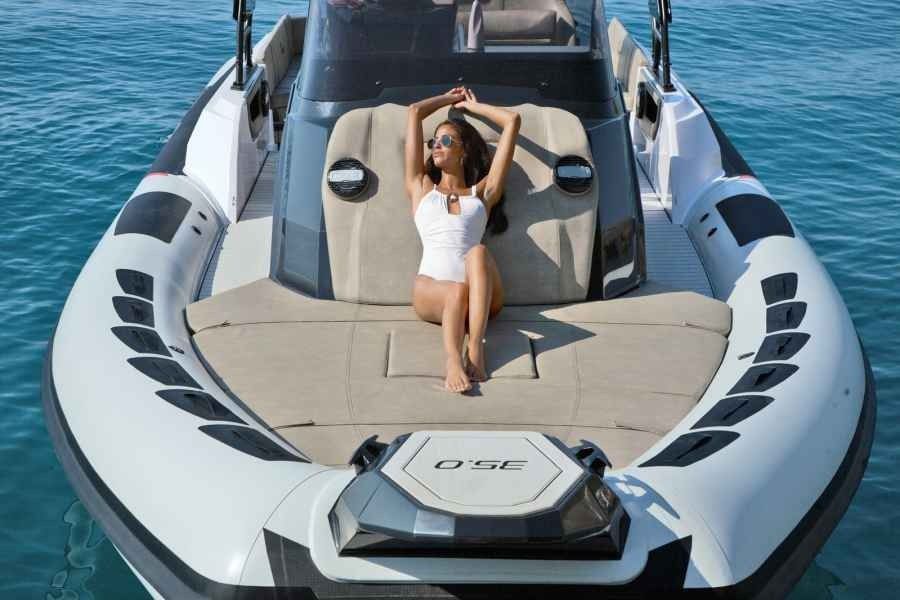 Person relaxing on the bow of a sleek white boat on blue water.