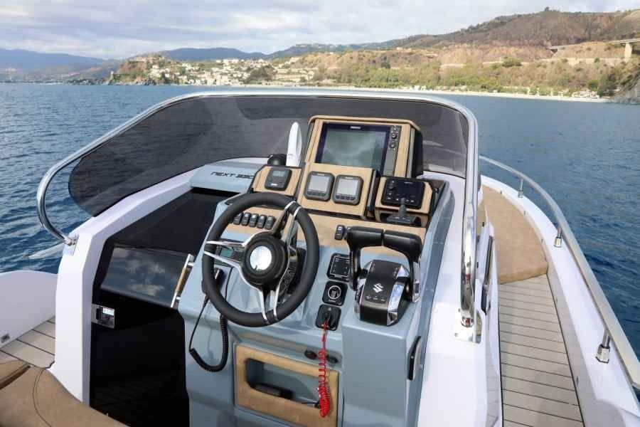 Boat helm with steering wheel and gauges on a yacht cruising on open water.
