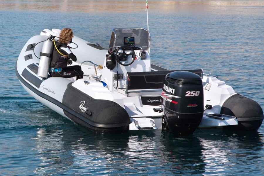 Inflatable ranieri cayman 23 sport diving rib motorboat on calm water with a person seated at the helm and a black outboard engine at the stern