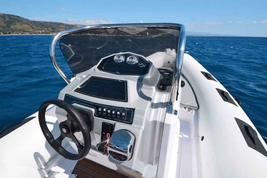 Boat helm and windshield on a speedboat, with open blue water and coastline ahead