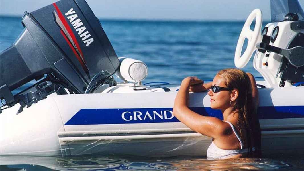 Woman in sunglasses relaxing in the water beside a Yamaha motorboat on a sunny sea.
