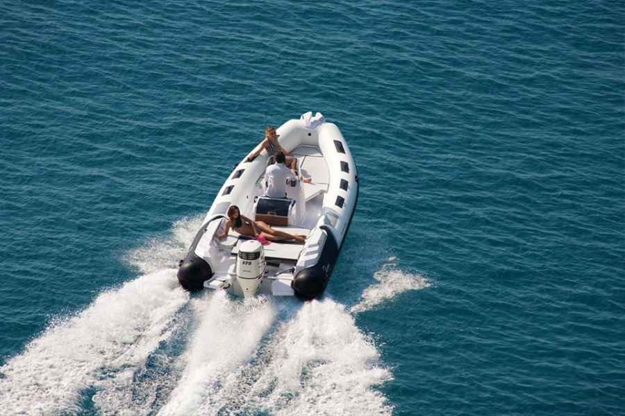 Small white motorboat speeding across blue water, leaving a foamy wake behind.