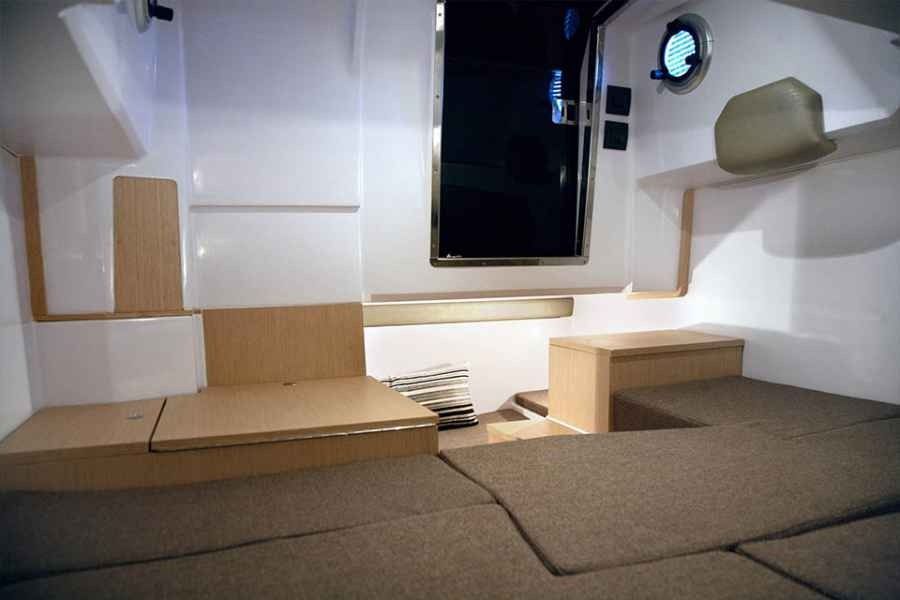 Small boat cabin interior with tan cushions, white walls, and a round window.