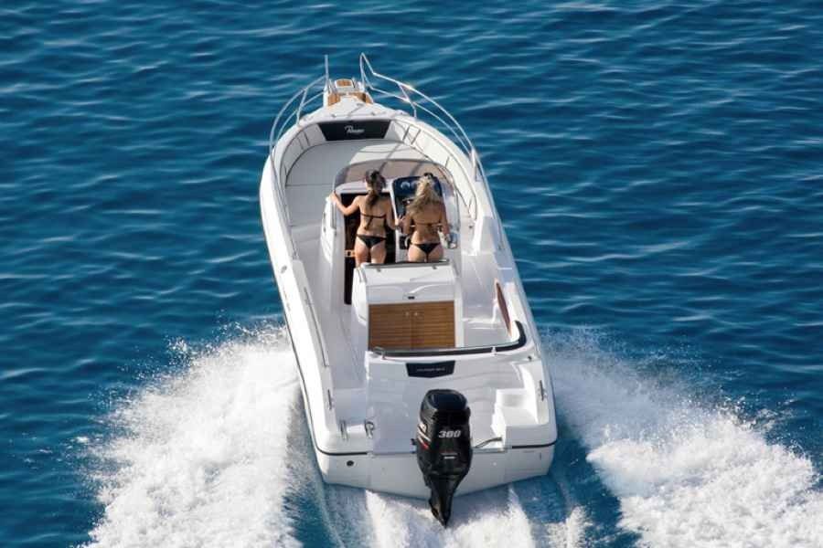 Small white motorboat speeding across blue water, with two people aboard and a wake behind it